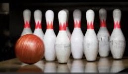 A bowling ball heading towards the pins at the end of an alley.