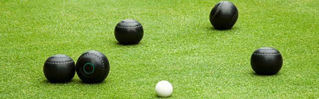 black balls on a flat green surrounding a white target ball.