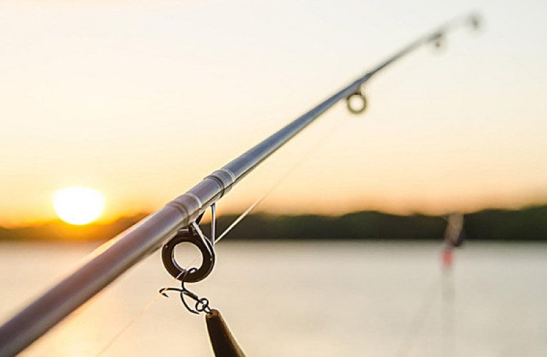 An image of a fishing rod in the foreground, with a sun setting in the background.